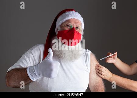 Santa Claus wearing face mask getting vaccinated with injection Stock Photo