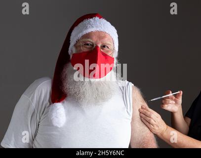Santa Claus wearing face mask getting vaccinated with injection Stock Photo