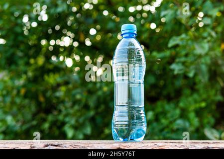 Drinking water pouring from a plastic bottle with blurry green foliage in the backdrop Stock Photo