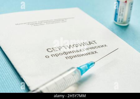 A document for recording vaccinations made in Russia, a syringe and a bottle of vaccine on a blue background. Translated from Russian: Certificate of Stock Photo