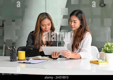 Beautiful young college students are looking at their work assignment questions on the digital tablet computer. Stock Photo