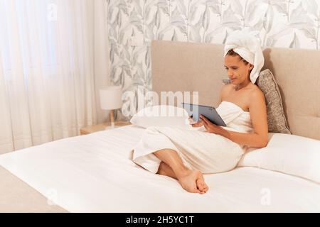 Woman wrapped in towels lying on bed using digital tablet Stock Photo