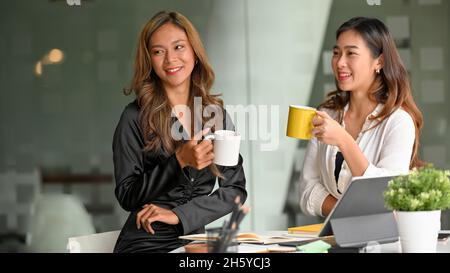 Two beautiful asian businesswomen enjoy talking during coffee break at the office break room. Stock Photo
