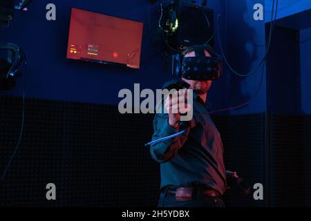 Young man in virtual reality helmet using joystick while playing new video game in vr club. Stock Photo