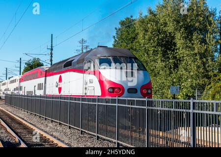 MP36PH-3C diesel locomotive in Caltrain livery, used for Baby Bullet service, belching out black diesel smoke while passing the station behind securit Stock Photo