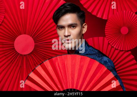 Handsome Asian man in tradition Chinese costume looking at cemera in oriental red folding fan background Stock Photo