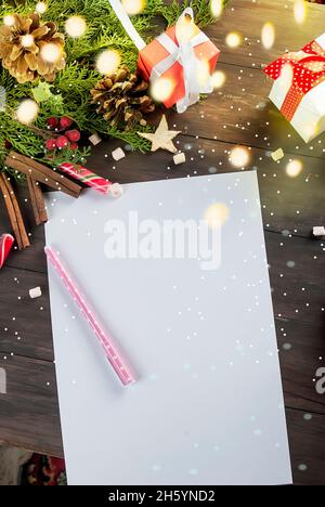 Top view of christmas letter in santa claus hand.  High angle view of santa claus hands writing on a paper with gift boxes and fir branch on table. Stock Photo