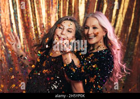 Two senior girlfriends having fun in studio blowing confetti Stock Photo
