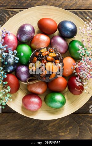 Easter cake with dried fruits and nuts on a large wooden plate with colored eggs. top view. vertical image Stock Photo