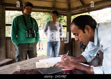November 2017. Nature guide, Rajendra Chaudhary (left), pays tourist entrance fees which contribute to the revenue generation in Kumrose Comunity Forest. He became a guide six years ago after graduating with a humanities degree from university. He love being out in and learning about nature. Jeep safaris are replacing elephant safaris in Chitwan National Park and some of the community forests, catering to tourists more sensitive to animal rights issues or who are simply looking for a diferent experience. Kumrose Community Forest, Kumrose, Nepal. Stock Photo