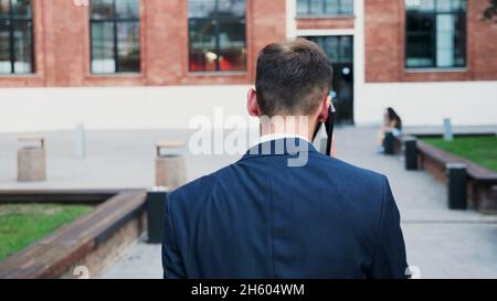 Back front of executive manager going to startup office building talking at phone with remote entrepreneur explaining company strategy while working at business presentation. Outdoors concept Stock Photo