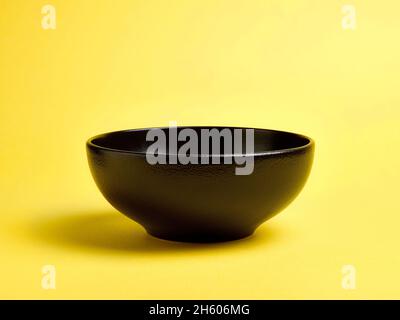 Empty black ceramic bowl on yellow background Stock Photo