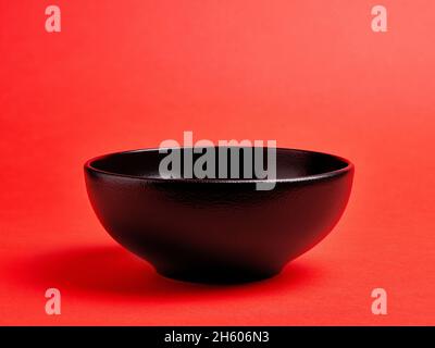 Empty black ceramic bowl on red background Stock Photo