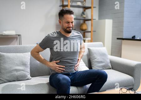 Man Suffering From Stomach Ache Sitting On Sofa Stock Photo