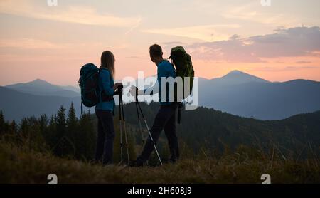 Couple of travelers watching surrounding scenery at sunset in mountains. Magic sky in different shades of pink color over mountain peaks in the evening. Concept of travelling, hiking, relationships. Stock Photo