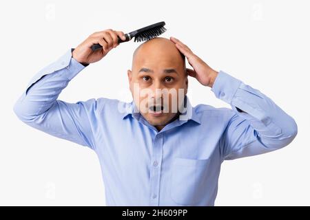 Portrait of a bald man combing his shaved head while gaping against white background. Stock Photo