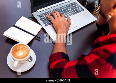 hand of an unrecognizable man typing on a laptop computer at a coffee shop table, concept of technology and urban lifestyle Stock Photo