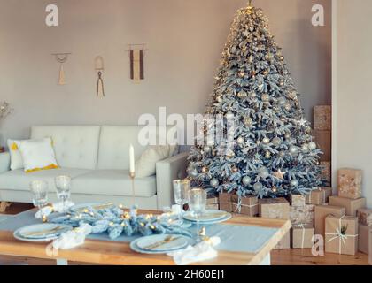 Bright living room decorated with New Year decor. Christmas tree with gold and silver decorations and lots of wrapped gift boxes under it. Christmas t Stock Photo