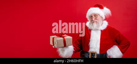 Banner real funny Santa Claus with gift present box on hand on red studio background. Sale, Discount, Black Friday. Copyspace Stock Photo