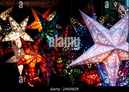 Glowing Christmas lanterns in star shape from folded paper in a market booth at night, selling light for the dark winter holidays, copy space, selecte Stock Photo