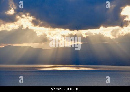 Sun Rays pouring through the clouds into the sea. Crepuscular rays. Sun rays on golden hour to the sea. Colorful, partially cloudy orange sunset with Stock Photo
