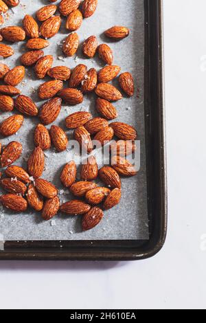 Raw almonds prepared with olive oil, sea salt and smoked paprika on a baking tray ready for roasting. Stock Photo