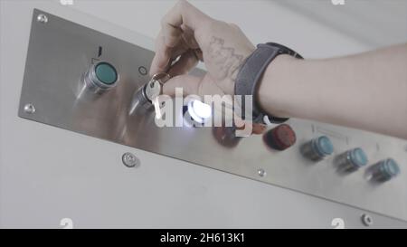 Egineer turns key on control panel. Action. Close-up of worker's hand turns power key for operation of industrial equipment. Control panel with key on Stock Photo
