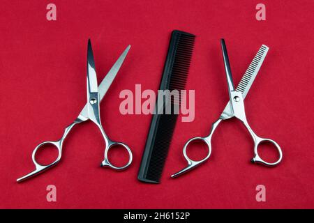 Hairdressing scissors and shears with comb on a red table surface Stock Photo