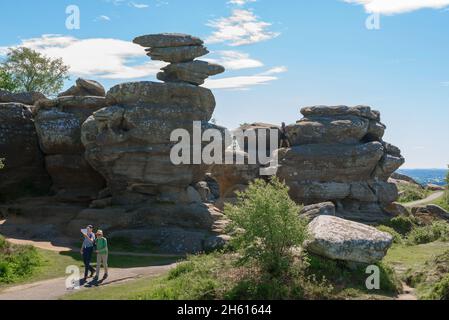 Brimham Rocks, view in summer of a senior couple walking past a heavily eroded rock formation at Brimham Rocks in Nidderdale, North Yorkshire, England Stock Photo