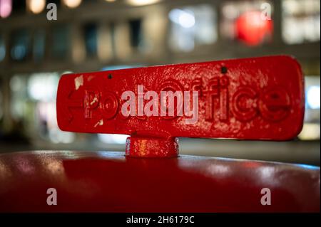 A sign on top of a traditional British Red Post Box pointing towards a post office Stock Photo