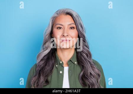 Photo of pretty charming lady pensioner dressed green shirt smiling isolated blue color background Stock Photo