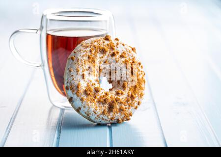 Sweet glazed donut with sprinkles and tea on blue kitchen table. Stock Photo