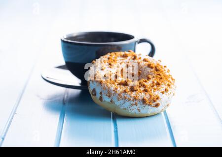 Sweet glazed donut with sprinkles and coffee cup on blue kitchen table. Stock Photo