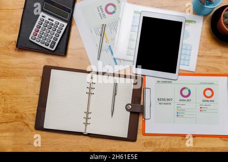 Top view of digital tablet with business paper chart or graph  and etc on wooden table. Wooden office desk with office supplies. Stock Photo