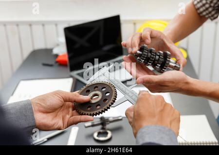 The engineering team is working on their project together. Man work with caliper measure the motor gear, engine part. Stock Photo