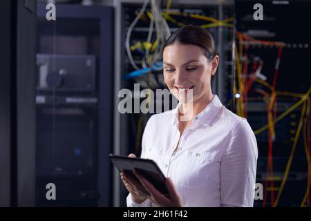 Caucasian female engineer smiling while using digital tablet in computer server room Stock Photo