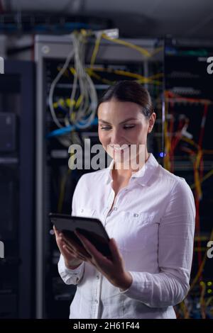 Caucasian female engineer smiling while using digital tablet in computer server room Stock Photo