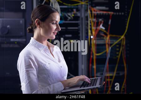 Caucasian female engineer using laptop in computer server room Stock Photo