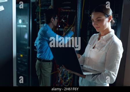 Caucasian female engineer using laptop and asian male engineer inspecting in computer server room Stock Photo