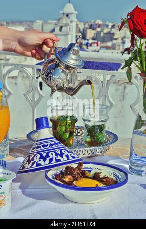 a woman holding in hand silver vintage teapot and pouring traditional mint sweet moroccan tea. Arabian hospitality and service. Stock Photo