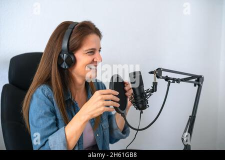Mature woman recording a podcast using microphone and headphones from her home studio Stock Photo