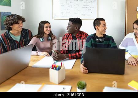 Young multiracial students reading books and using laptop in classroom while studying together - School education concept Stock Photo
