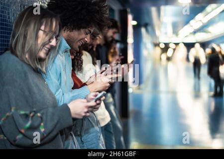 Young people using mobile smartphone in subway station waiting train - Youth millennial addicted to new technology concept Stock Photo