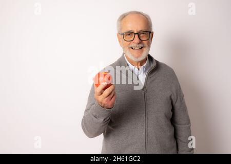 Senior happy man wearing casual sweater eating an apple isolated over white background. Stock Photo