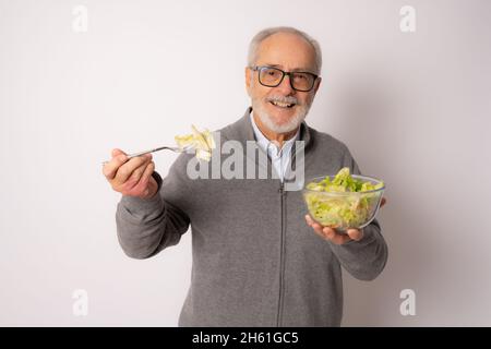 Senior happy man wearing casual sweater eating salad isolated over white background. Stock Photo