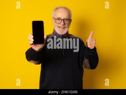 Lifestyle, technology and old people concept: Handsome old gray-haired man dressed in smart casual style using a smartphone and smiling over yellow ba Stock Photo