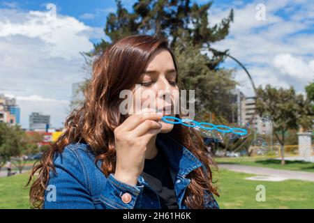 Close up view of beautiful Hispanic woman blowing soap bubbles in the middle of a park on a sunny morning Stock Photo