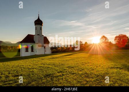 The Baroque chapel of St. Johann above the Loisach Valley and the autumnal Bavarian Alps with Zugspitze in the backlight of the evening sun, Germany Stock Photo