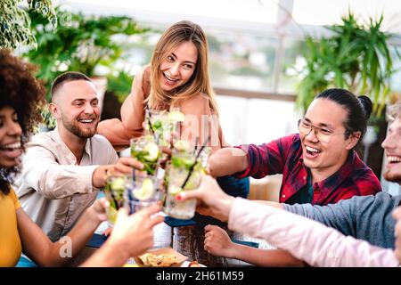 Young friends toasting mojito drinks at rooftop cocktail bar - Party time concept with multicultural people having fun drinking on happy hour Stock Photo