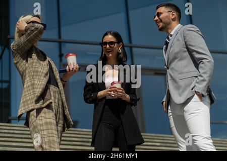 Three well suited business people are laughing while drinking coffee Stock Photo